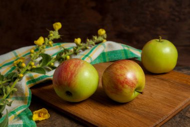 Tahta kesme tahtası, ahşap arka planda yeşil mutfak havlusuyla üç taze elma.