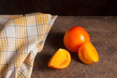 Eski ahşap arka planda kesilmiş, sulu sarı domates ve sarı havlu. Sebze koleksiyonu