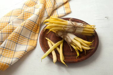 Birkaç kapsül ve ahşap beyaz arka planda sarı mutfak havlusu olan iki adet çiğ sarı kayısı kapsülü. Fransız fasulyesi ya da Hindistan 'dan String fasulyesi olarak da bilinir. Sebze koleksiyonu.