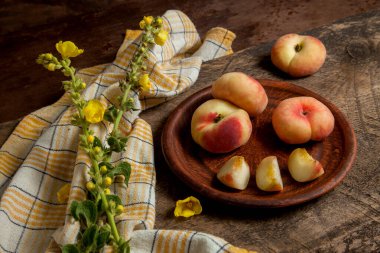 Çamur tabağı ve olgun Çin şeftali meyveleri ya da eski ahşap arka planda sarı mutfak havlusuyla satürn şeftali.