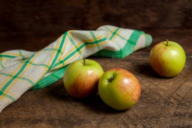 Ahşap arka planda yeşil mutfak havlusuyla üç taze elma.