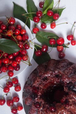Tatlı kirazlı lezzetli çikolatalı pasta, beyaz tepside tatlı kiraz ve beyaz arka planda yeşil kiraz ağacı yaprakları.