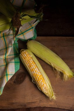 İki tane olgun mısır, yeşil yapraklar ve eski ahşap arka planda yeşil havlu. Beyaz ve sarı taneli koçanlar.