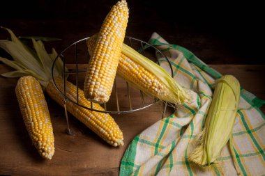 Birkaç tane olgun mısır ve eski ahşap arka planda yeşil havlu. Beyaz ve sarı taneli koçanlar. Arka planda yeşil yapraklı taze mısır kulakları.
