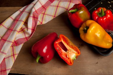 Kırmızı mutfak havlusuyla kırmızı ahşap arka planda kırmızı biber, tatlı dolma biber olarak bilinen tam ve yarı kırmızı ve sarı dolma biber.