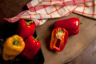 Kırmızı mutfak havlusuyla kırmızı ahşap arka planda kırmızı biber, tatlı dolma biber olarak bilinen tam ve yarı kırmızı ve sarı dolma biber.