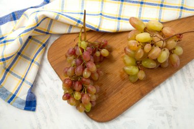 Beyaz üzerine olgun pembe üzümlerle tahta kesmek. Beyaz ahşap zemin üzerinde mavi mutfak havlusu olan pembe şarap üzümleri.