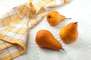 Beyaz ahşap arka planda çeşitli olgun armut meyveleri ve sarı mutfak havlusu.