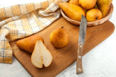 Ahşap kesme tahtası ve yarımşar yarımlık sulu armut meyvesi, armut sepeti ve beyaz ahşap arka planda sarı mutfak havlusu.