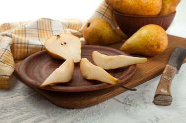 Dilimlenmiş kil tabağı ve yarım olgun armut meyvesi, armutlu hasır sepet ve ahşap kesim tahtasının üzerinde sarı mutfak havlusu.