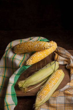 Birkaç tane olgun mısır ve eski ahşap arka planda yeşil havlu. Beyaz ve sarı taneli koçanlar. Arka planda yeşil yapraklı taze mısır kulakları.