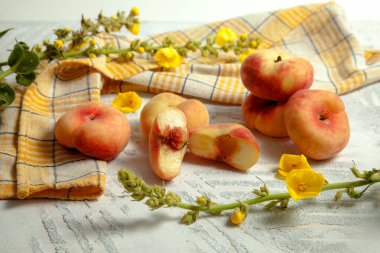 Yarım porsiyon ve bir sürü olgun Çin şeftali meyvesi ya da sarı mutfak havlusu ve sarı çiçekli klasik beyaz ahşap arka planda satürn şeftali.