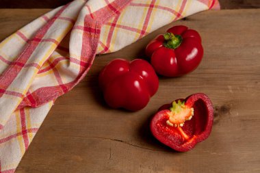 İki tam ve yarısı kırmızı dolma biber (capsicum) tatlı dolma biber olarak bilinir, kırmızı mutfak havlusuyla ahşap arka planda kırmızı biber.