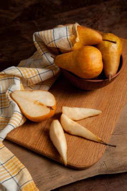 Tahta kesme tahtası dilimler ve yarım olgun sulu armut meyvesi, armutlu kil kase ve eski ahşap arka planda sarı mutfak havlusu.