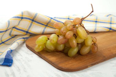 Beyaz üzerine olgun pembe üzümlerle tahta kesmek. Beyaz ahşap zemin üzerinde mavi mutfak havlusu olan pembe şarap üzümleri.