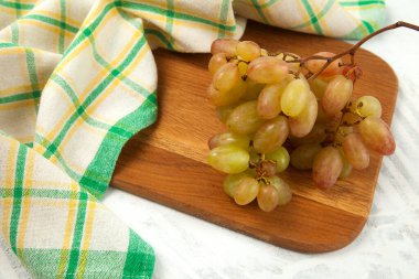 Beyaz üzerine olgun pembe üzümlerle tahta kesmek. Beyaz ahşap zemin üzerinde mavi mutfak havlusu olan pembe şarap üzümleri.