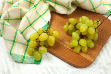 Beyaz üzerine olgun yeşil üzümlerle tahta kesmek. Beyaz ahşap arka planda yeşil mutfak havlusu olan beyaz şarap üzümleri.