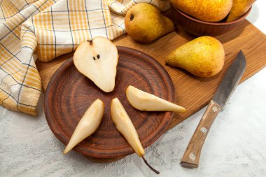 Dilimlenmiş kil tabağı ve yarım olgun armut meyvesi, armutlu hasır sepet ve ahşap kesim tahtasının üzerinde sarı mutfak havlusu.