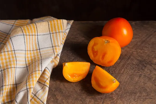 Eski ahşap arka planda kesilmiş, sulu sarı domates ve sarı havlu. Sebze koleksiyonu