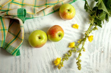 Yeşil mutfak havlusuyla beyaz ahşap arka planda üç taze yeşil elma.