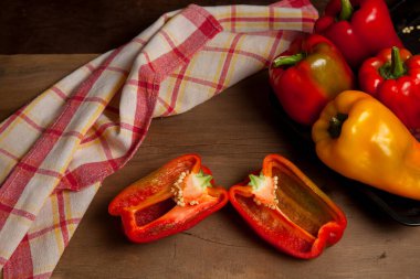 Kırmızı mutfak havlusuyla kırmızı ahşap arka planda kırmızı biber, tatlı dolma biber olarak bilinen tam ve yarı kırmızı ve sarı dolma biber.