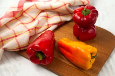 Beyaz ahşap zemin üzerinde tatlı dolma biber, paprika ve kırmızı mutfak havlusu olarak bilinen kırmızı ve sarı dolma biberli kesme tahtası.