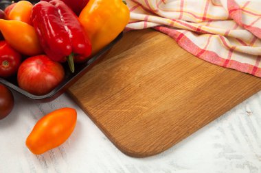 Sebze arkaplan resmi. Tahtadaki sebzelerle dolu bir kase. İçinde çeşit çeşit olgun domatesler ve kırmızı mutfak havlusuyla beyaz ahşap arka planda dolma biber var.