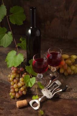 Lezzetli bir alkollü içecek, şarap ve üzüm konsepti. Şarap şişesi, mantar, tirbuşon, kırmızı şarap bardakları ve üzümlü, koyu, ahşap arka planda üzüm yapraklı üzümler.