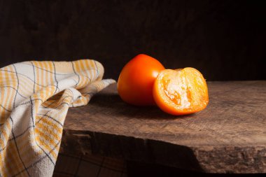 Kaliteli ahşap arka planda tam ve yarım porsiyon sulu sarı domates ve sarı havlu. Sebze koleksiyonu