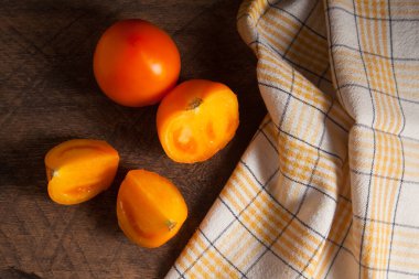 Eski ahşap arka planda kesilmiş, sulu sarı domates ve sarı havlu. Sebze koleksiyonu