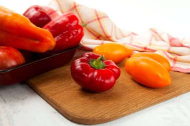 Tahtadaki sebzelerle dolu bir kase. İçinde çeşit çeşit olgun domatesler ve kırmızı mutfak havlusuyla beyaz ahşap arka planda dolma biber var.