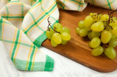 Beyaz üzerine olgun yeşil üzümlerle tahta kesmek. Beyaz ahşap arka planda yeşil mutfak havlusu olan beyaz şarap üzümleri.