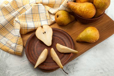 Dilimlenmiş kil tabağı ve yarım olgun armut meyvesi, armutlu hasır sepet ve ahşap kesim tahtasının üzerinde sarı mutfak havlusu.