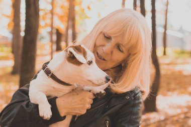 Sonbahar parkında köpeğini kucaklayan kıdemli bir kadın. Etkin yaşlanma ve evcil hayvan konsepti