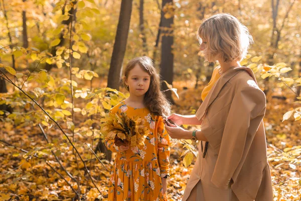Worried mom looking at offended little daughter after family argument in autumn nature, mother and female child suffering misunderstanding and conflicts at home problems between child and parent