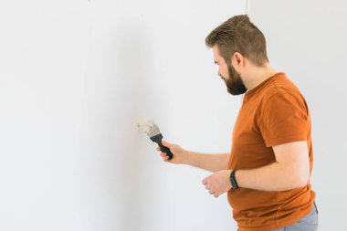 Genç adam spatula kullanıyor ve duvara beyaz taze macun yapıştırıyor. - Yakın çekim. Ev onarımı. Mesaj için boş bir yer. Yan görünüm