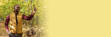 Sonbahar sonbahar parkında Afro-Amerikalı bir adam akıllı telefonuyla kendi portresini çekiyor. Mutlu insanlar, mevsim ve yeni normallik