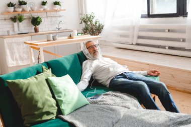 Son sınıf hipster 'ı cep telefonuyla mobil uygulama üzerinden müzik dinlerken kullanıyor. Yaşlı erkek video akıllı telefon izlerken yüz koruyucu maske takıyor.