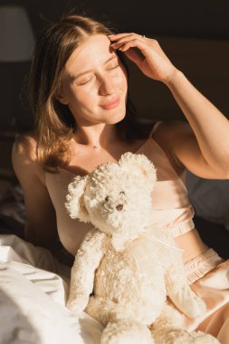 Kız sabah uyanıyor yatakta esneme hareketleri yapıyor ve pencereden güneş parlıyor. Mutlu kadın yeni güneşli günü selamlıyor