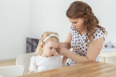 Mother helps her deaf baby daughter putting hearing aid in little girls ear indoors - cochlear implant and innovative medical technologies