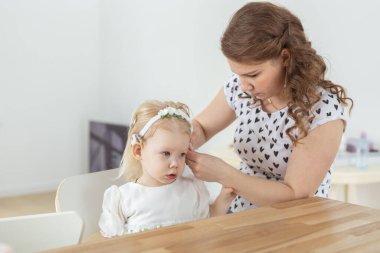 Mother helps her deaf baby daughter putting hearing aid in little girls ear indoors - cochlear implant and innovative medical technologies