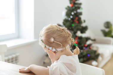 Child girl dressed in christmas dress with cochlear implants having fun at home - hearing aid and innovating technologies for treatment deafness