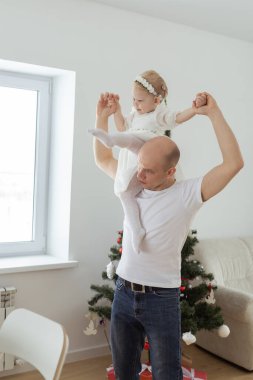 İşitme cihazı ve koklear implantı olan bebek Noel ağacı arka planında babasıyla eğleniyor. Sağırlık, çeşitlilik ve sağlık