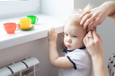 Mother fixing her daughters cochlear implant hearing aid - deafness and diversity concept. Innovative technologies in treatment deafness