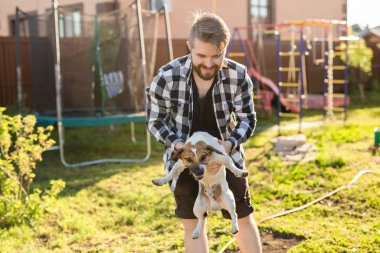 Genç adam beyaz Jack Russell Terrier köpeği tutuyor. Parkta kafasında kahverengi lekeler var.