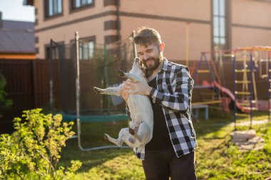 Genç adam beyaz Jack Russell Terrier köpeği tutuyor. Parkta kafasında kahverengi lekeler var.