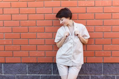 Evdeki neşeli kadın pijamasını giyer tuğla duvar arkası duyguları - pijama ve ev kıyafetleri