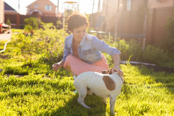 stock image Young woman plays with her dog on the grass on backyard. The concept of animals and friendship or pet owner and love.