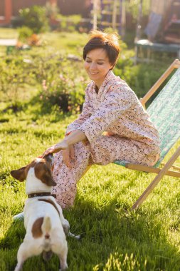 Young woman in pajama is resting in chair on a green lawn on sunny summer day - village and country life