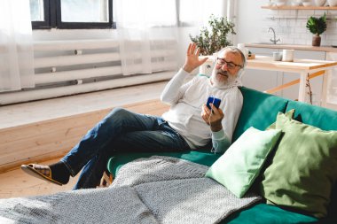 Yaşlı adam, havalı sakallı yaşlı adam video görüşmesi için cep telefonu kullanıyor. Mutluluk, yaşlılar yaşam tarzı kavramı. Akıllı telefondan çocuklara el sallayıp sohbet eden bir video. Modern.